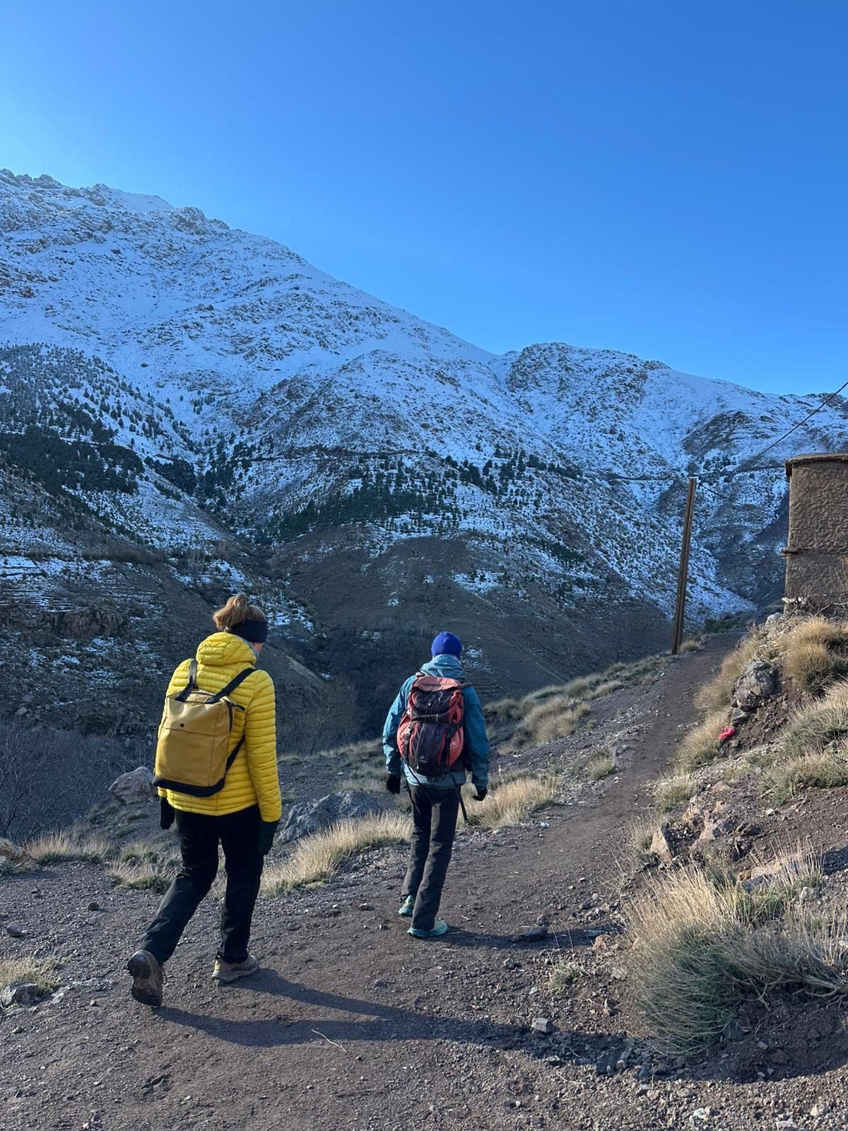 Two hikers on a trail below snow-dusted Atlas peaks
