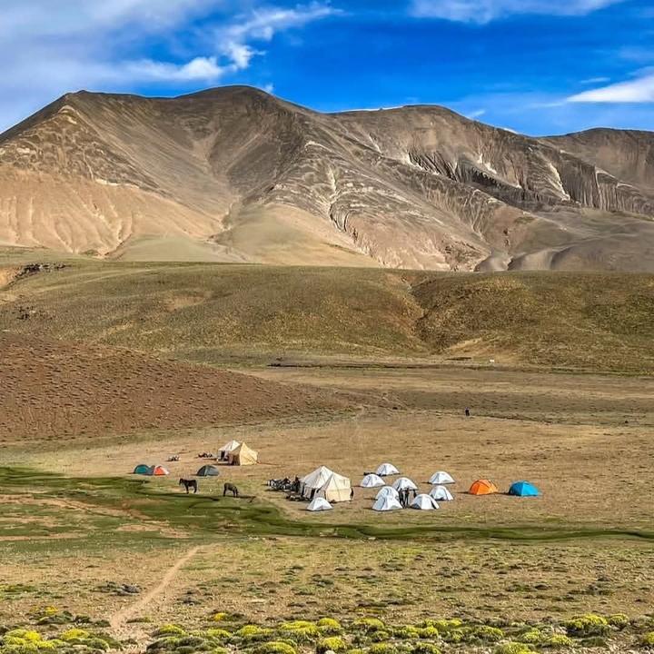 A trekking camp of tents on a high plateau below bare mountains