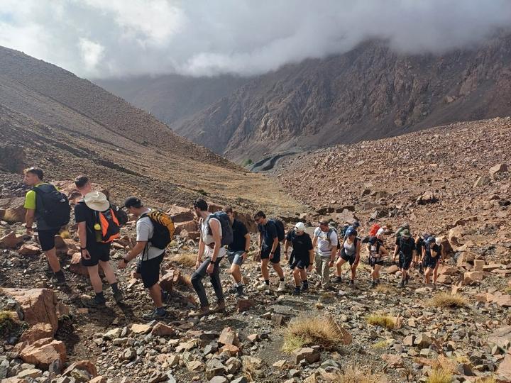 A group of trekkers climbing a rocky slope beneath low cloud