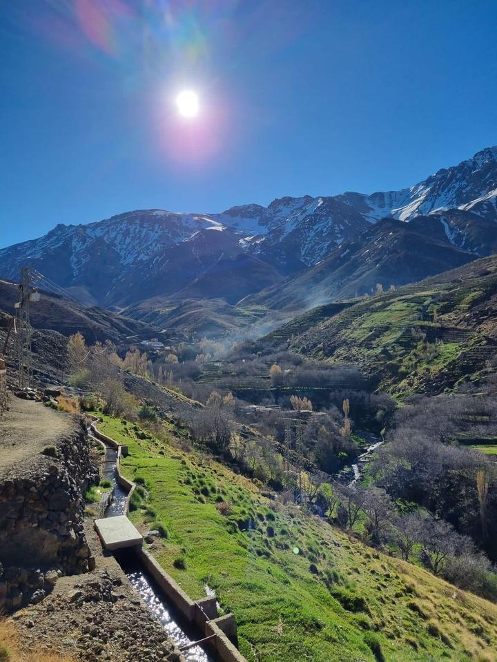 A stone irrigation channel running through a green valley below snow-capped peaks